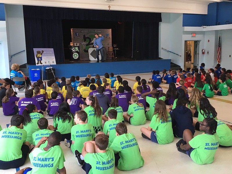 Kids in a school pay attention to a man talking about recycling

